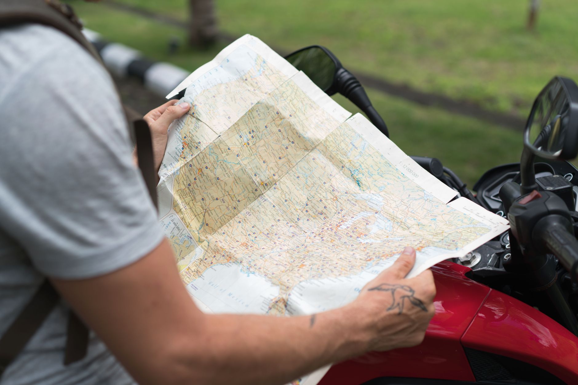 Vue de côté d'un voyageur anonyme dans des vêtements décontractés avec un sac à dos assis sur une moto tout en étudiant une carte de la ville dans la rue